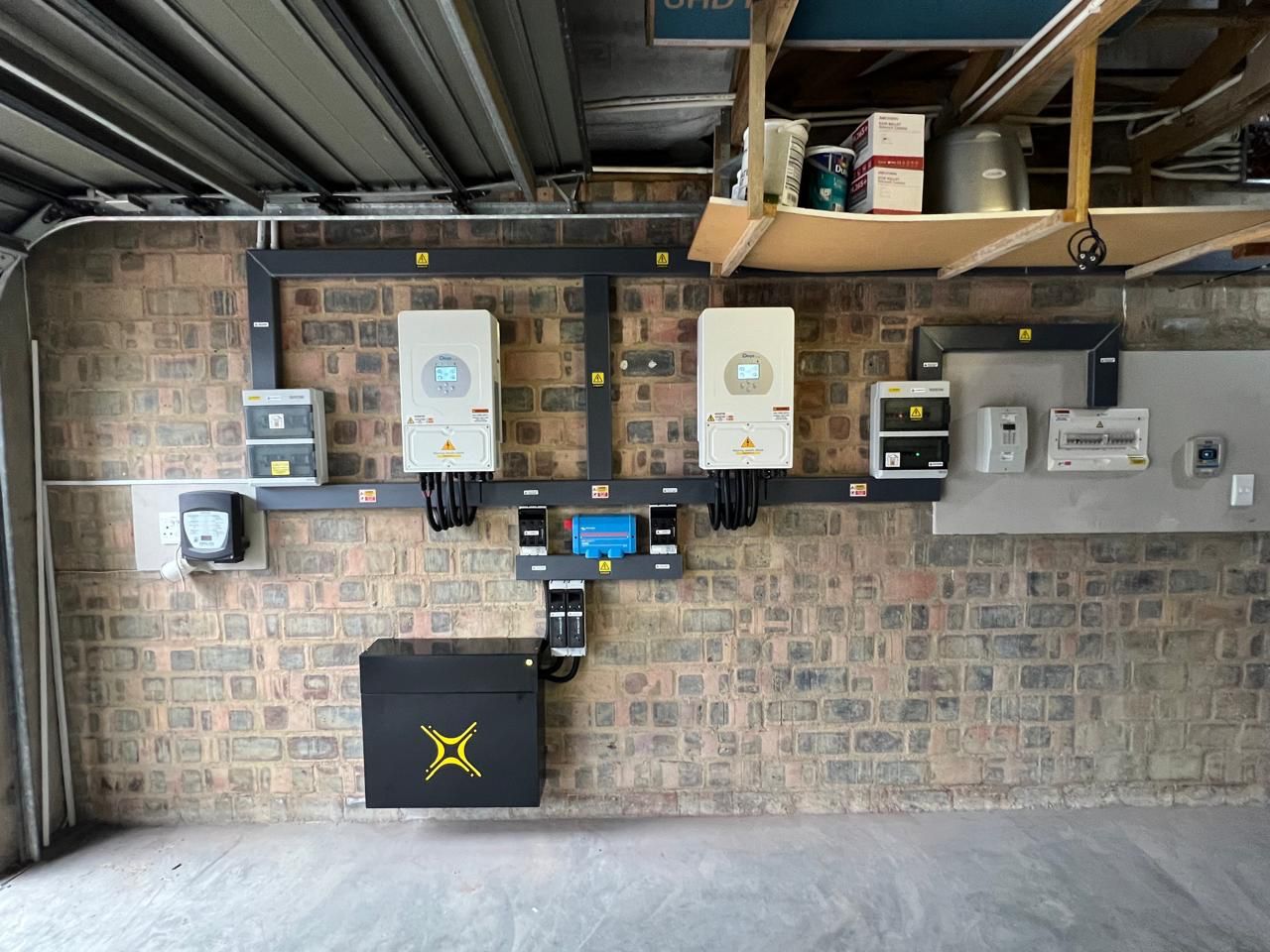 Two inverters and a wall-mounted battery installed on a brick garage wall