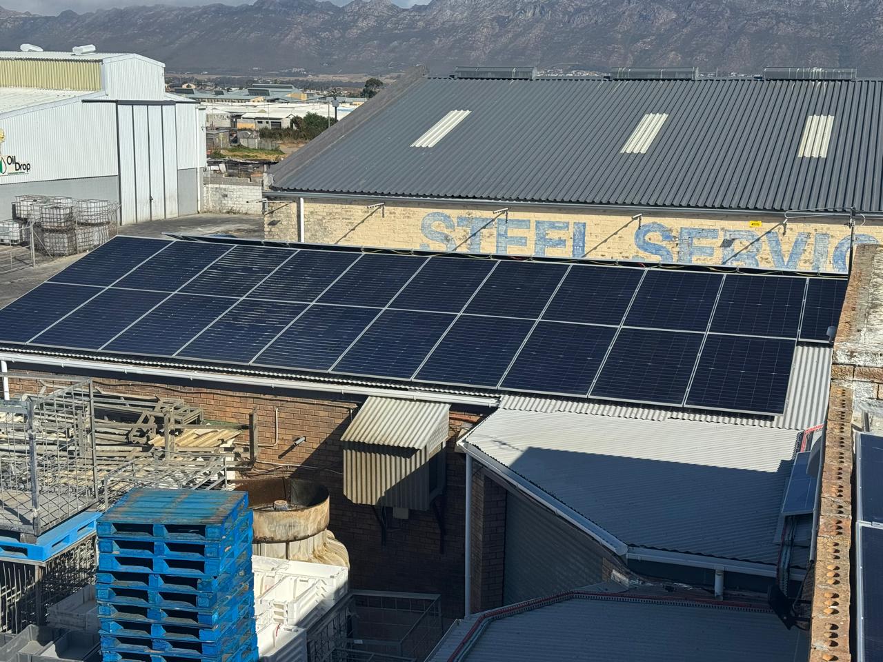 Rows of solar panels on a commercial roof with mountains behind