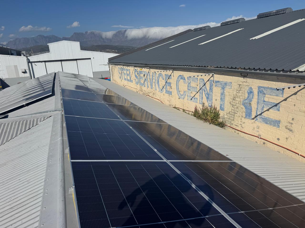 Solar panels installed along a sloping metal roof beside a commercial building
