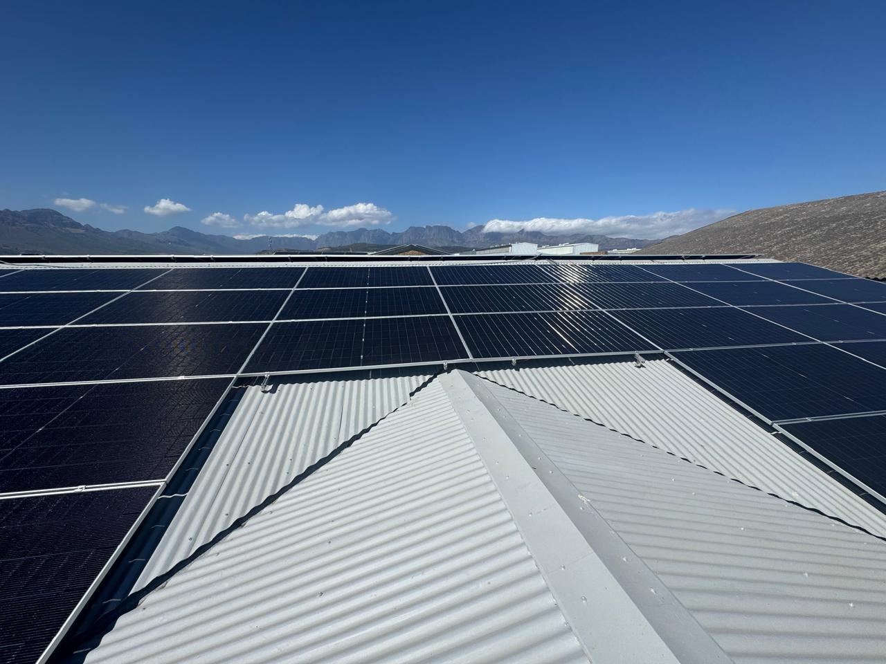 Solar panels across a metal roof with mountains in the distance